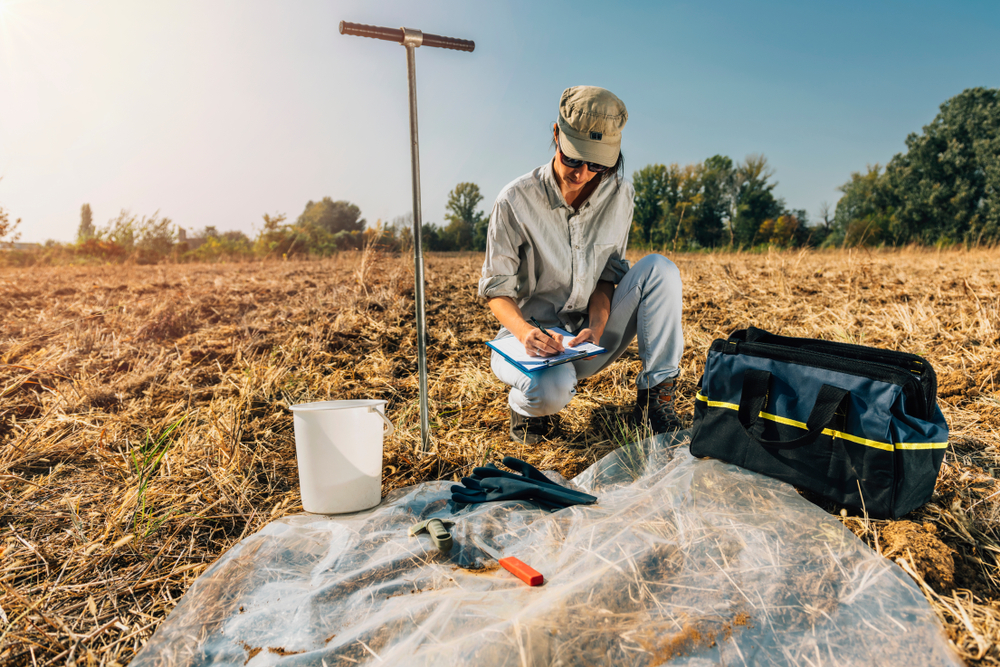Soil probe in ground with sample bag and clipboard, hands-on soil sampling in the field