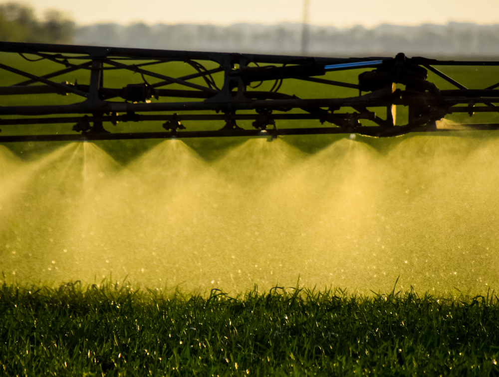 Foliar spray boom misting a field at golden hour