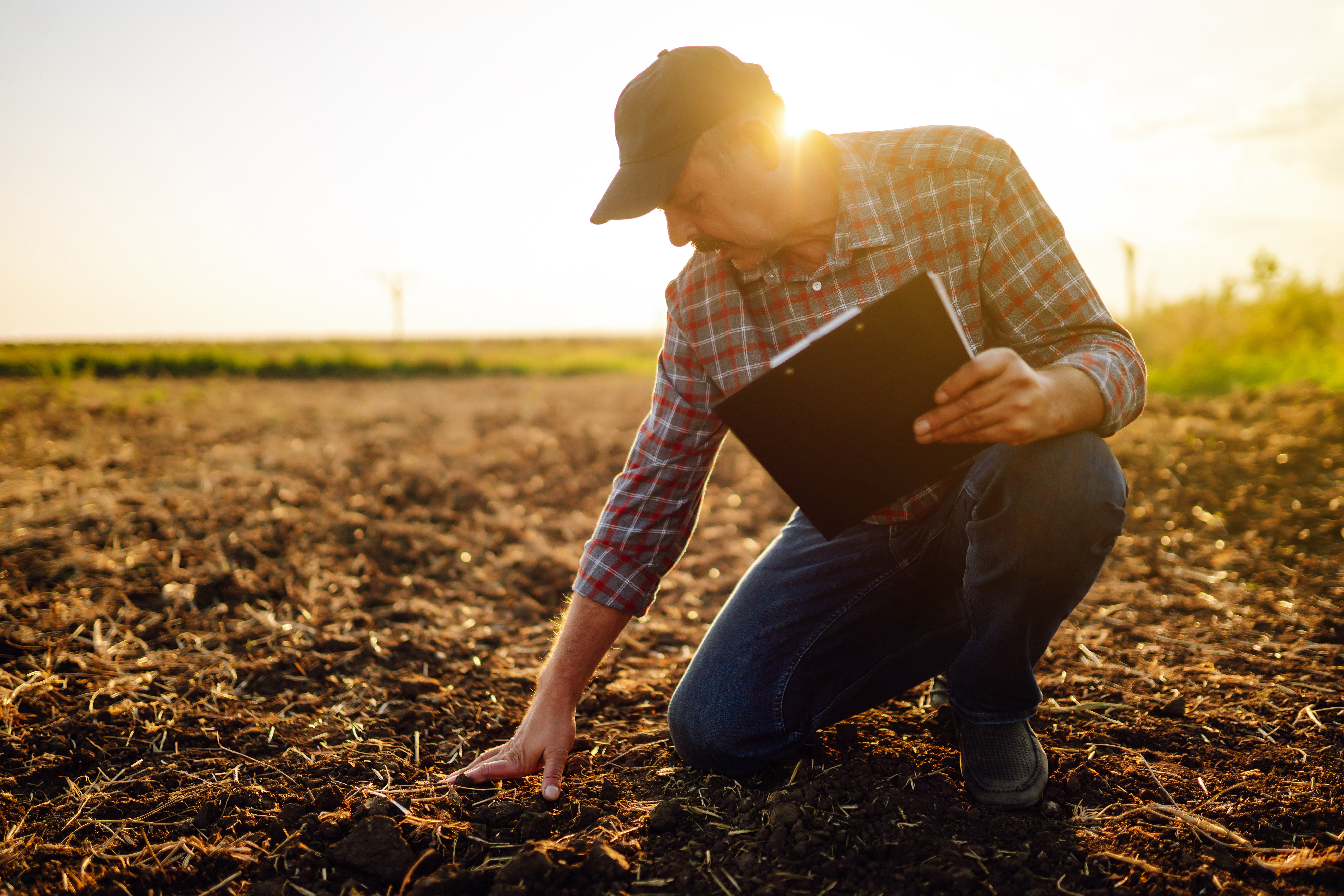 AgriTec agronomist crouched in a field at golden hour, examining soil